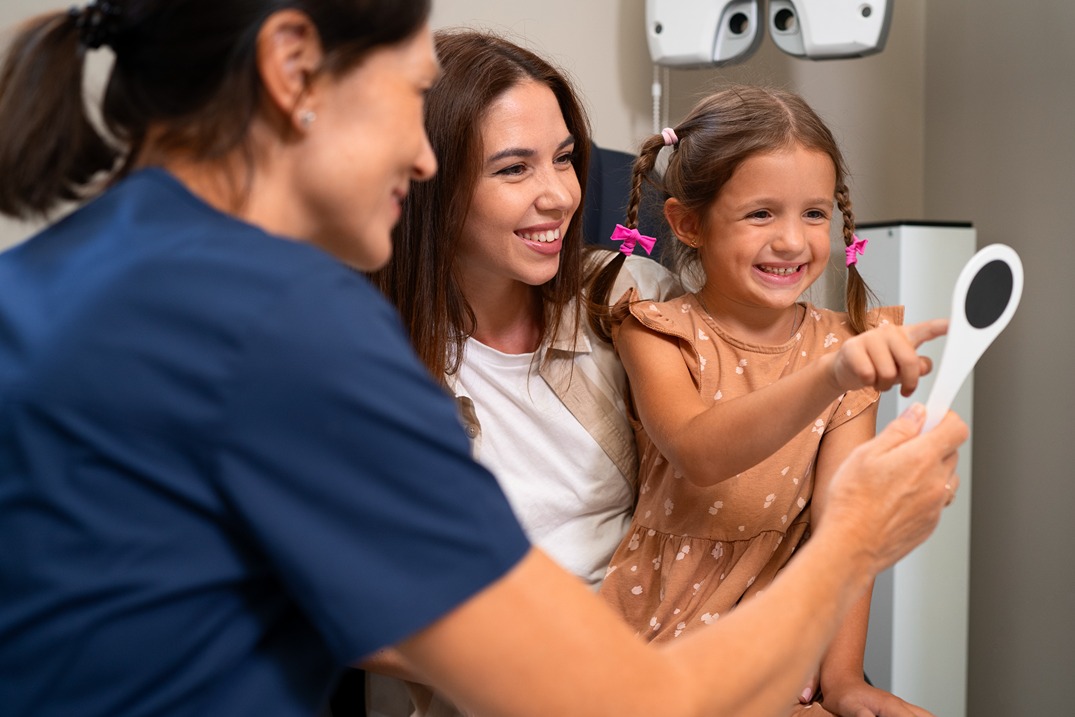 Young girl smiling during a dental checkup with her mother and dentist.